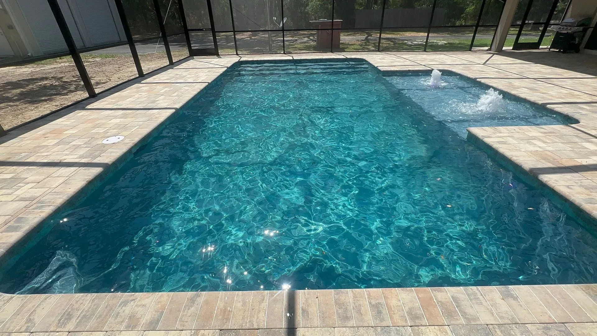Rectangular pool with attached spa, turquoise water, tan patio, and screened enclosure.