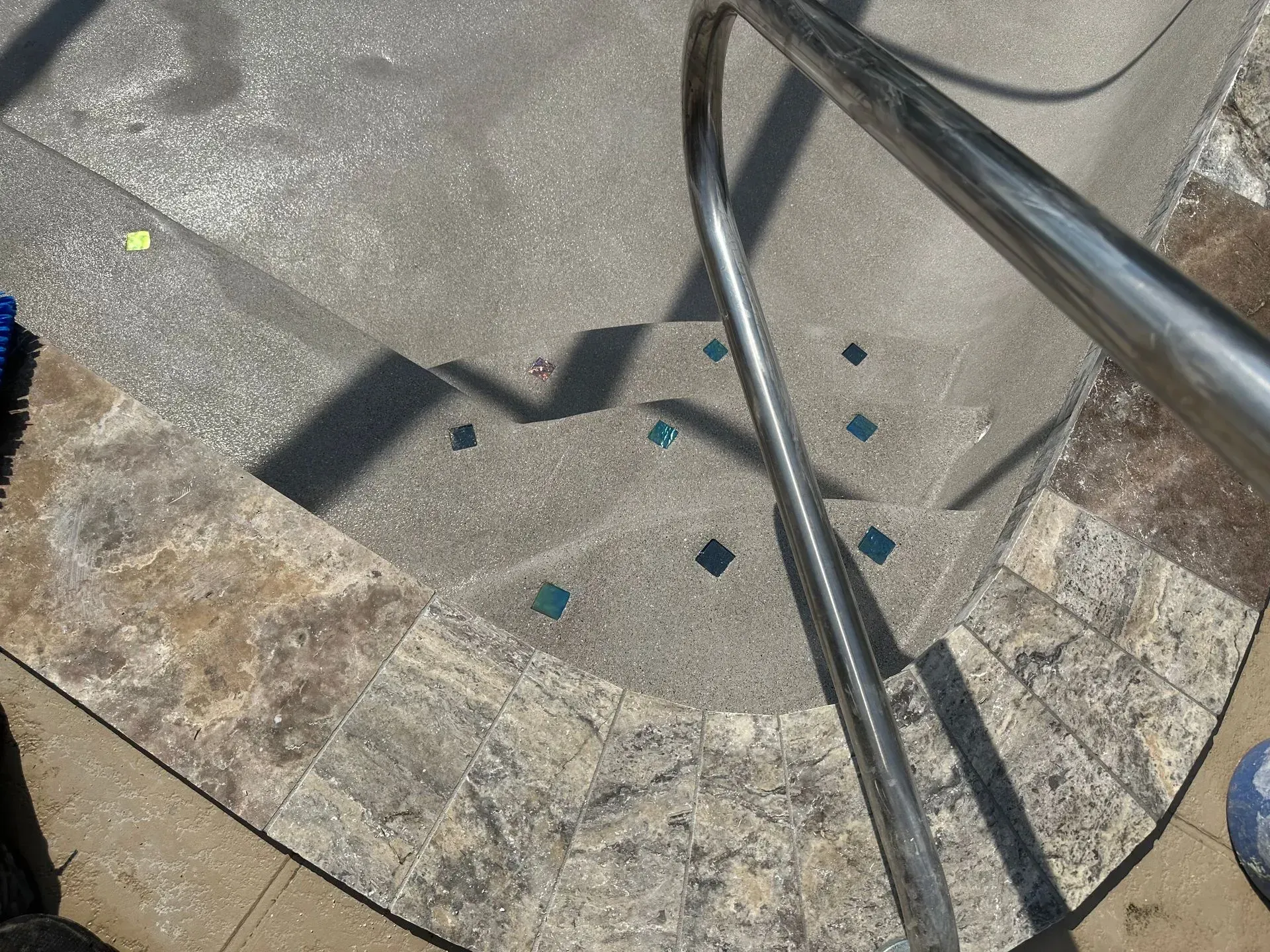 Pool steps with a metal handrail, decorated with small blue tiles and surrounded by stone.