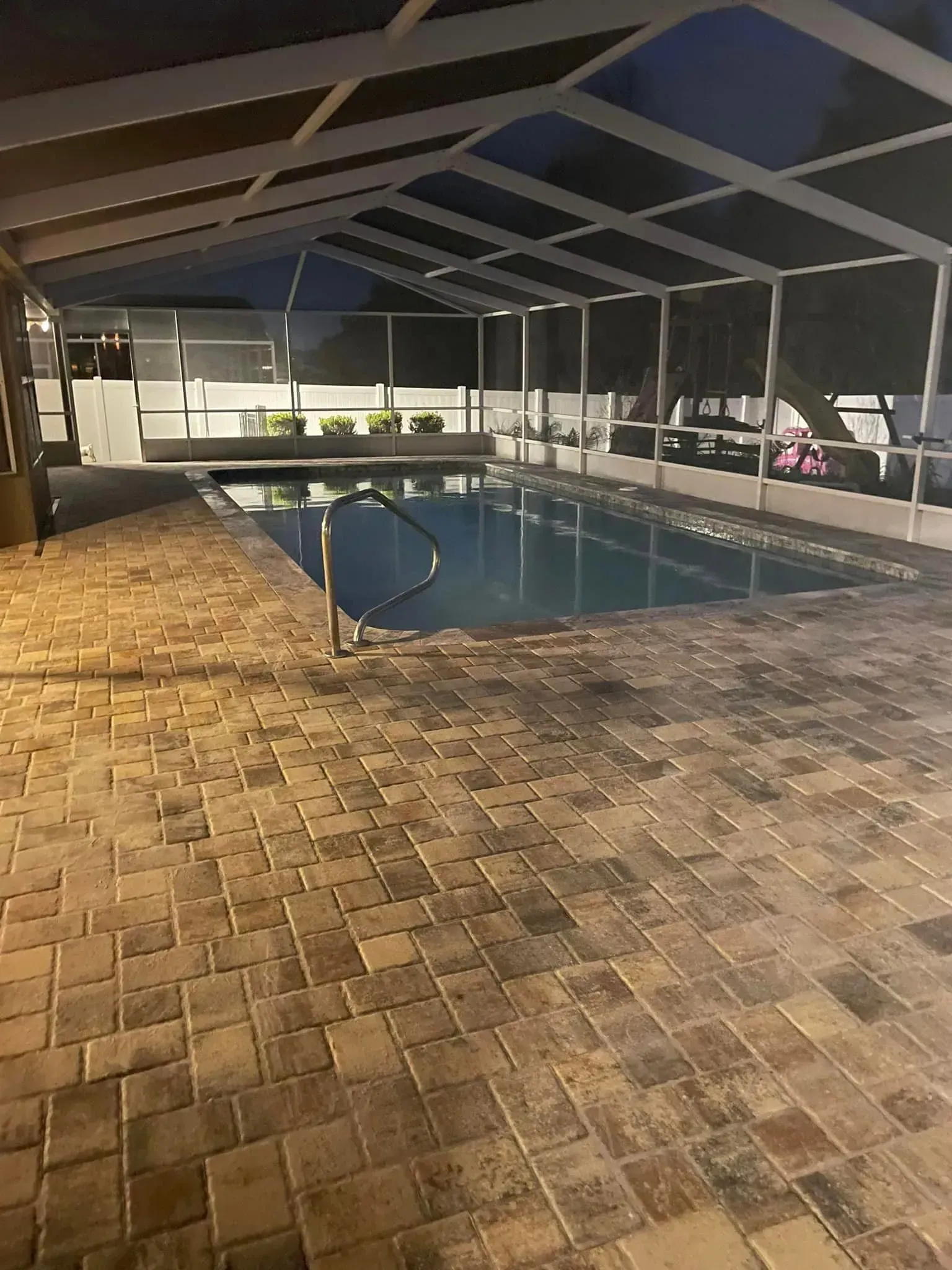 Pool enclosed in screened patio, brick pavers, dark lighting.