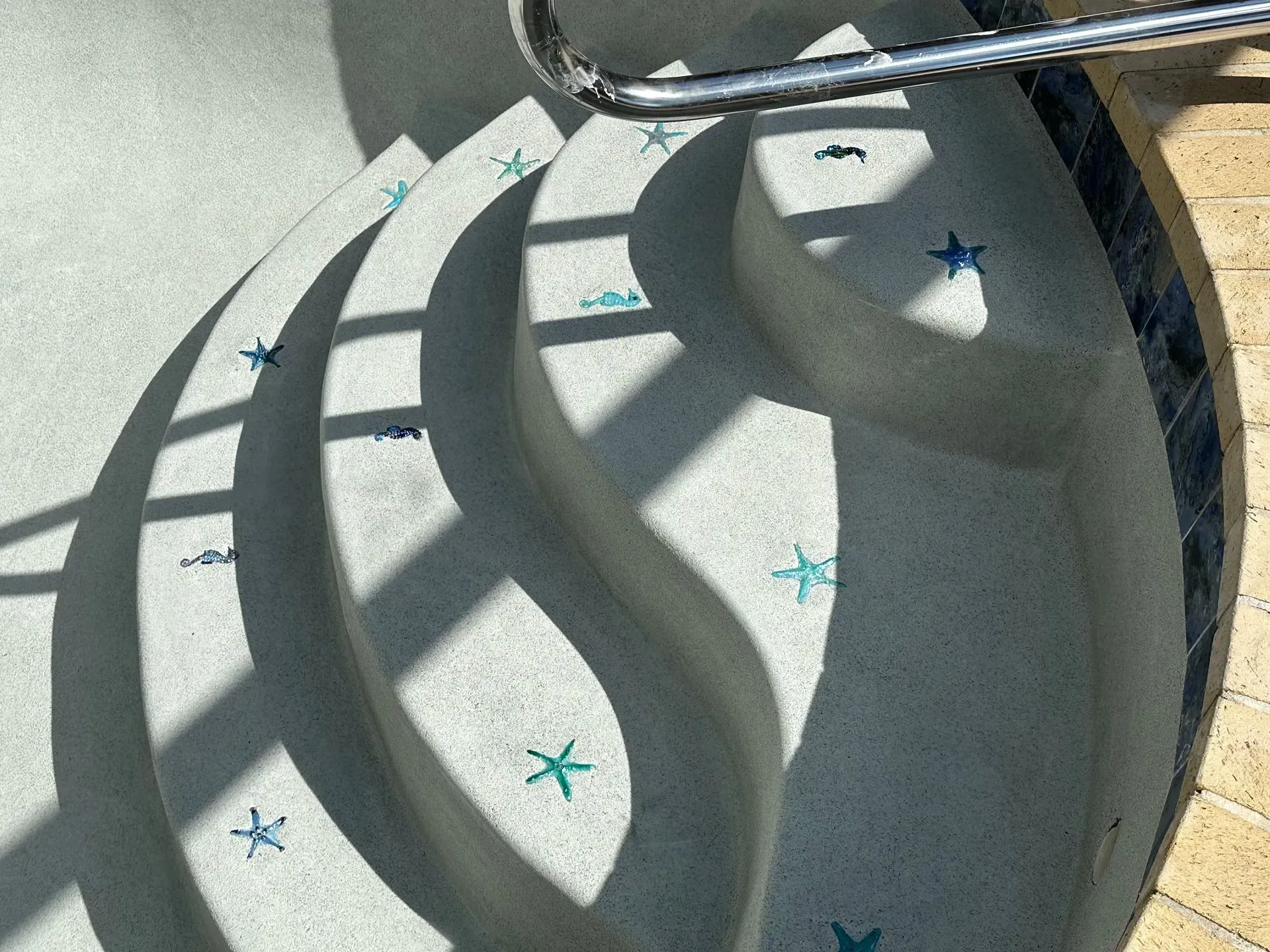 Pool steps with a handrail, decorated with starfish, in direct sunlight.