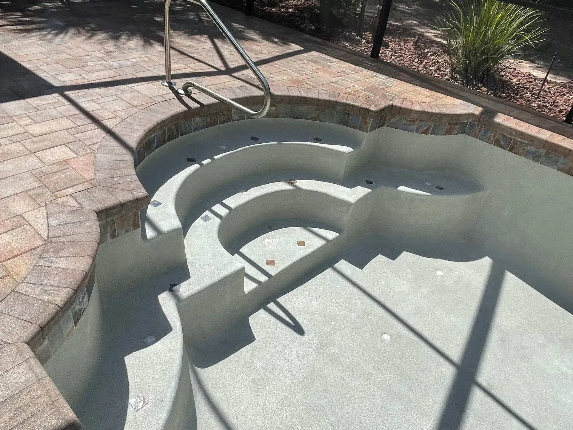 Pool steps leading into a partially filled pool with a handrail. Brick pavers surround the pool.