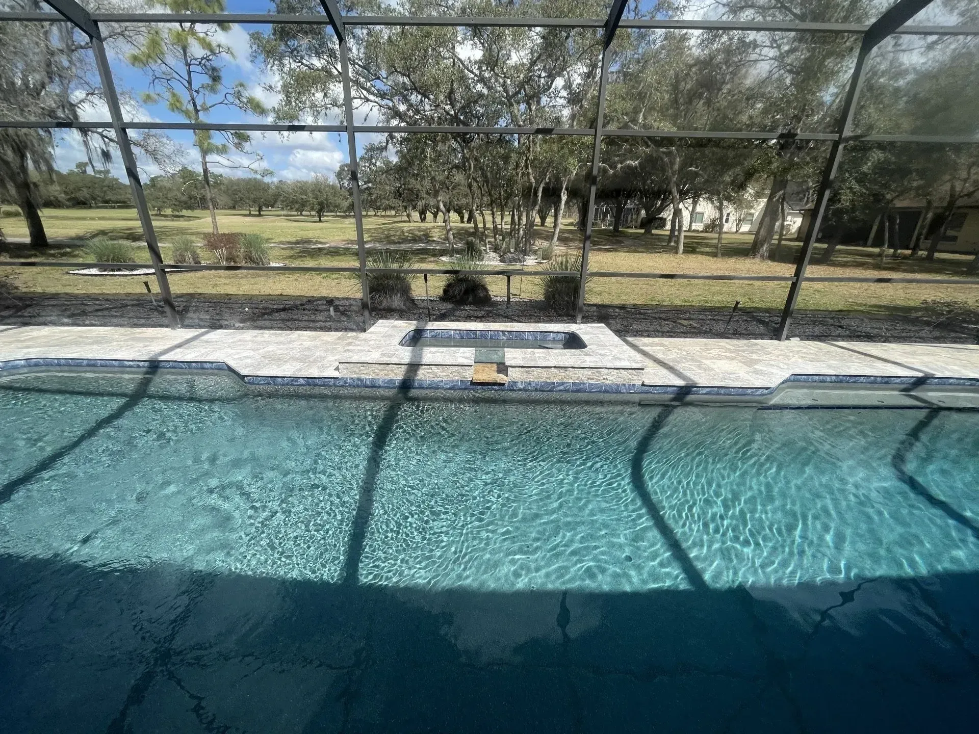 Pool with clear turquoise water and a screened patio overlooking a grassy backyard under a sunny sky.