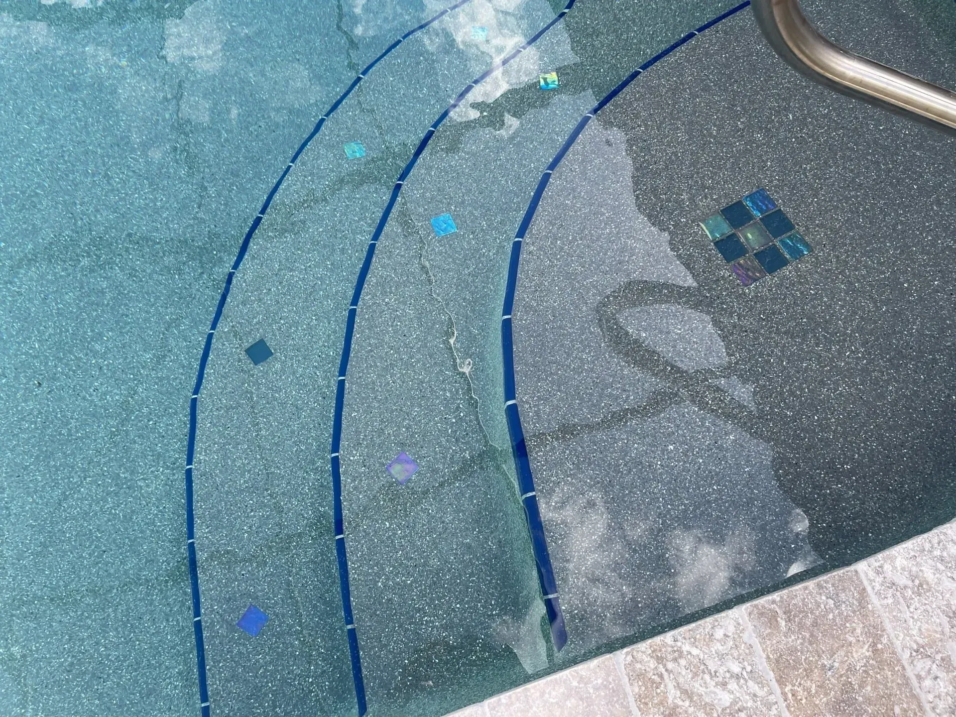 Pool steps with blue tile accents and scattered mosaic tiles.