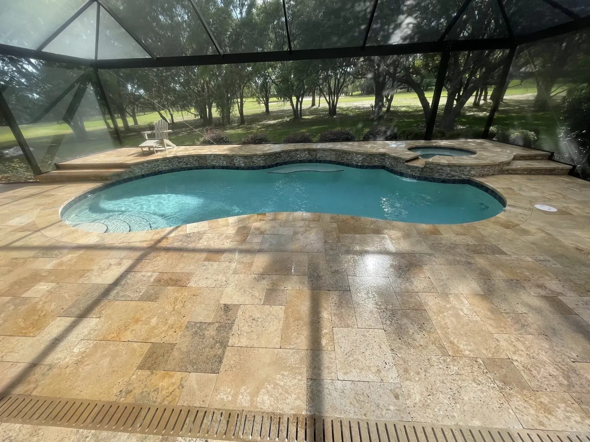 Pool area with a turquoise pool, spa, and light stone patio, enclosed by a screen.