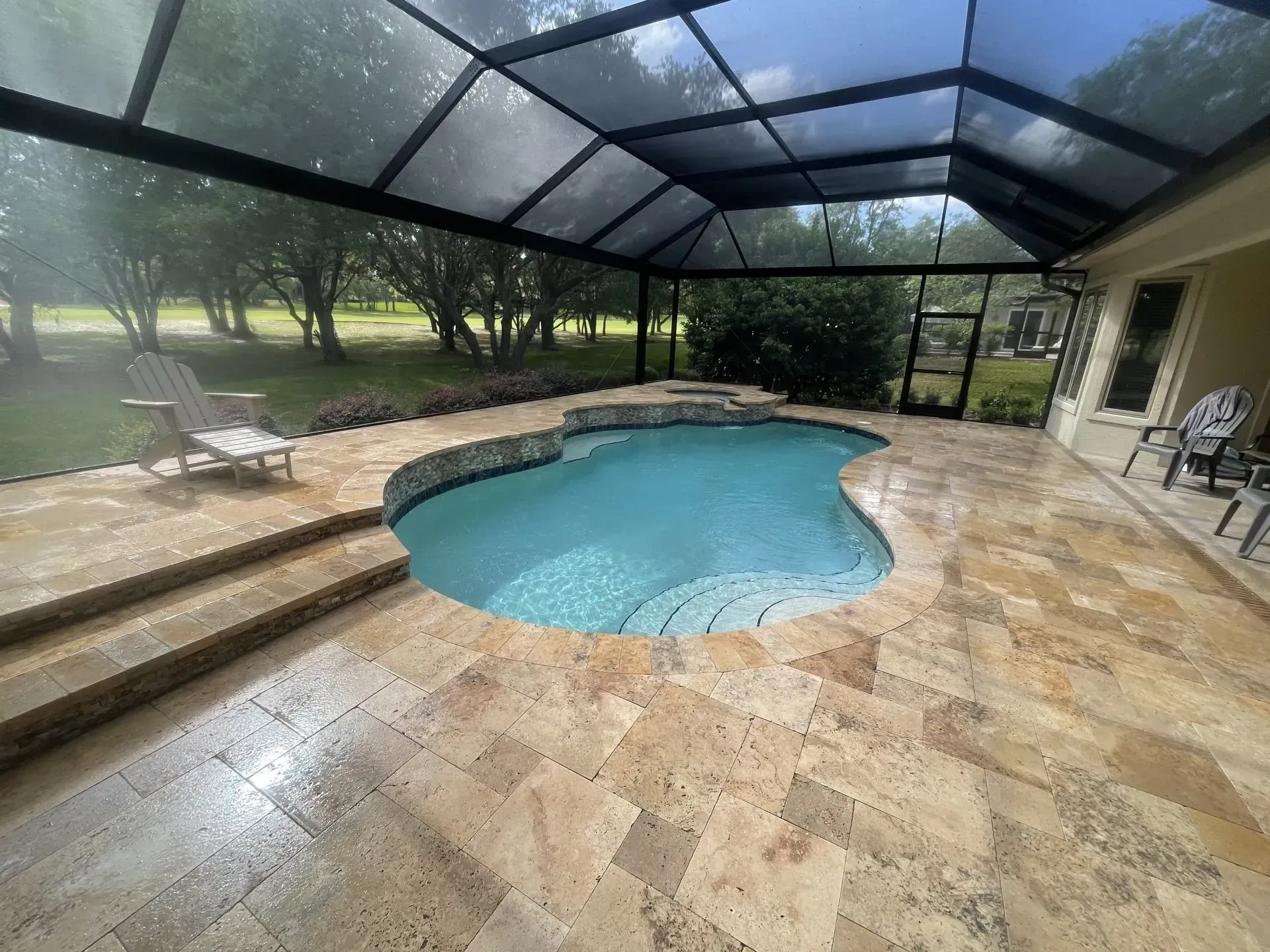 Pool enclosure with a swimming pool, stone patio, and chairs.
