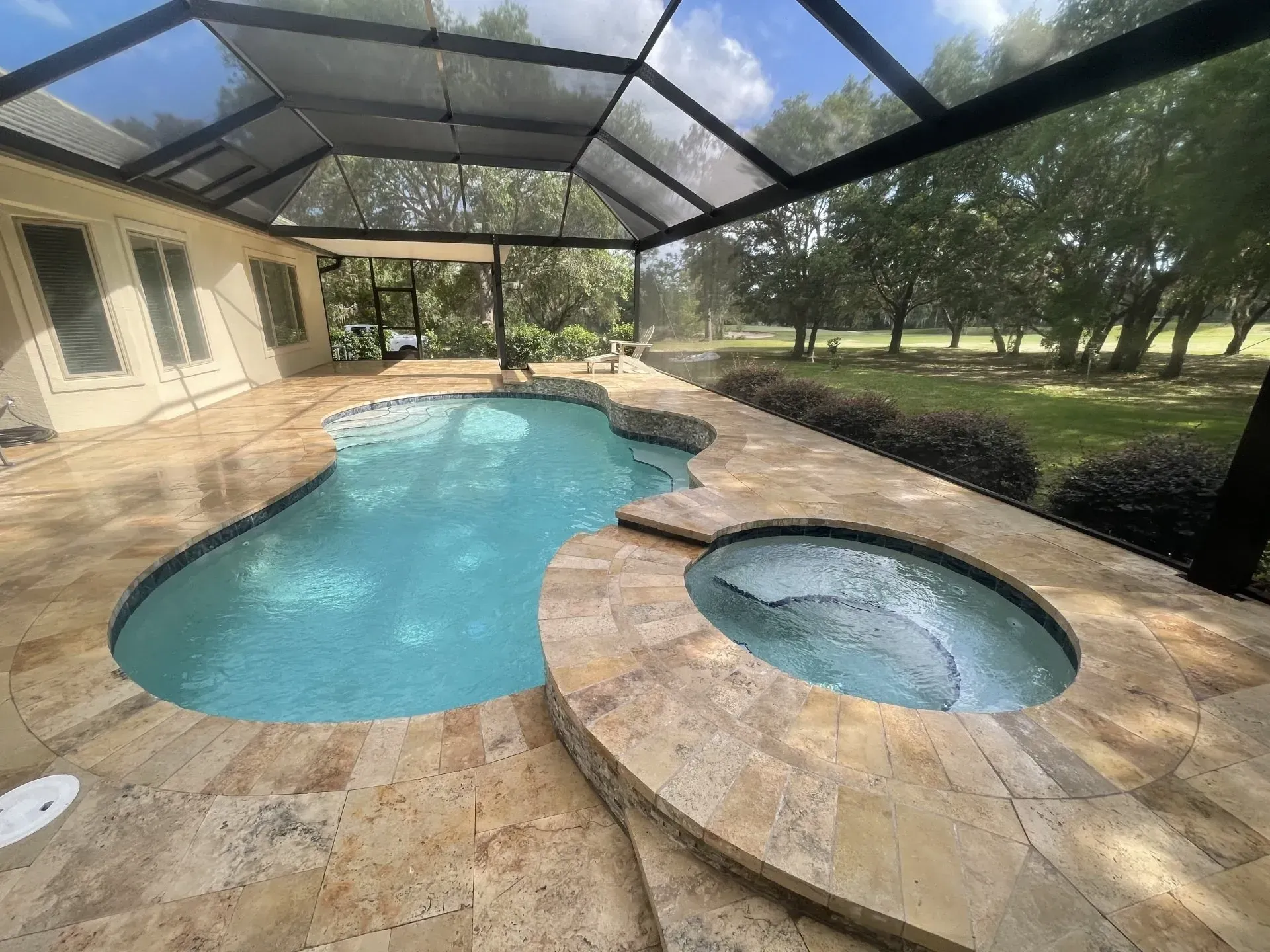 Swimming pool with attached jacuzzi on a stone patio, under a screened enclosure.