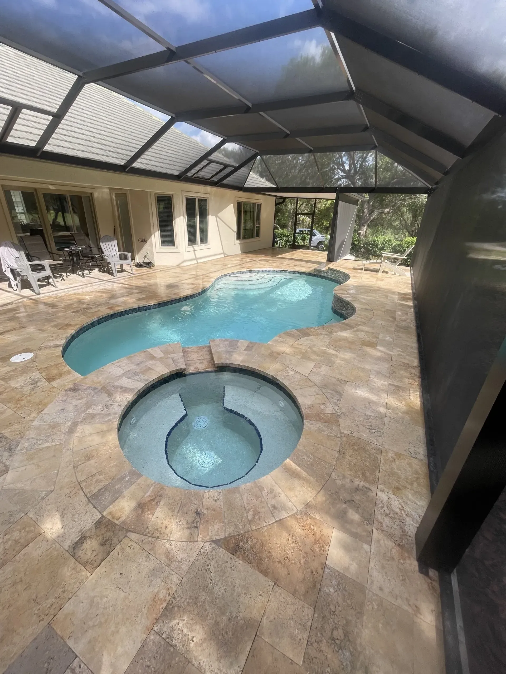 Pool and spa under screened enclosure; light blue water, beige stone surround.