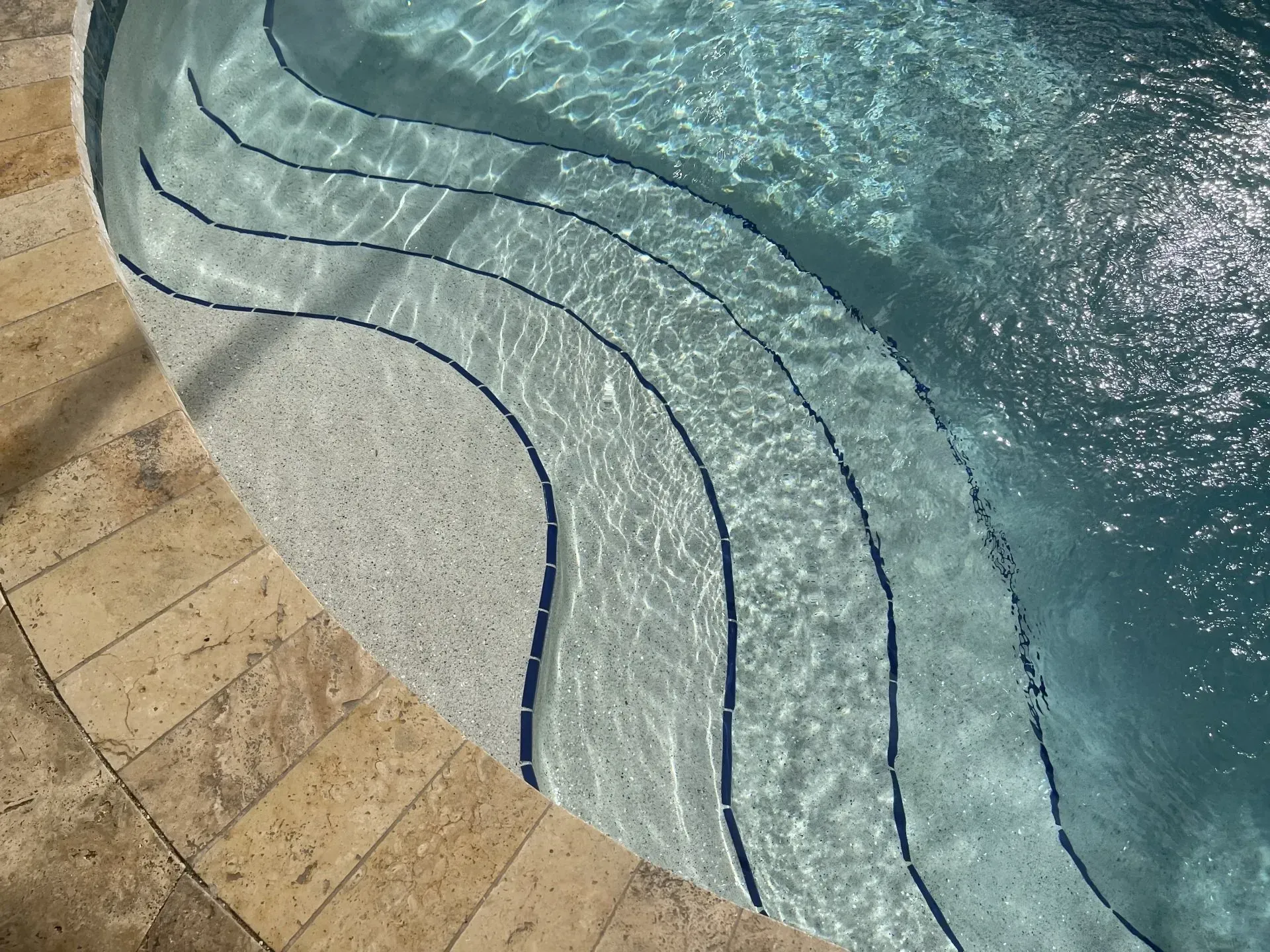 Steps leading into a swimming pool with light blue water and stone tiles.
