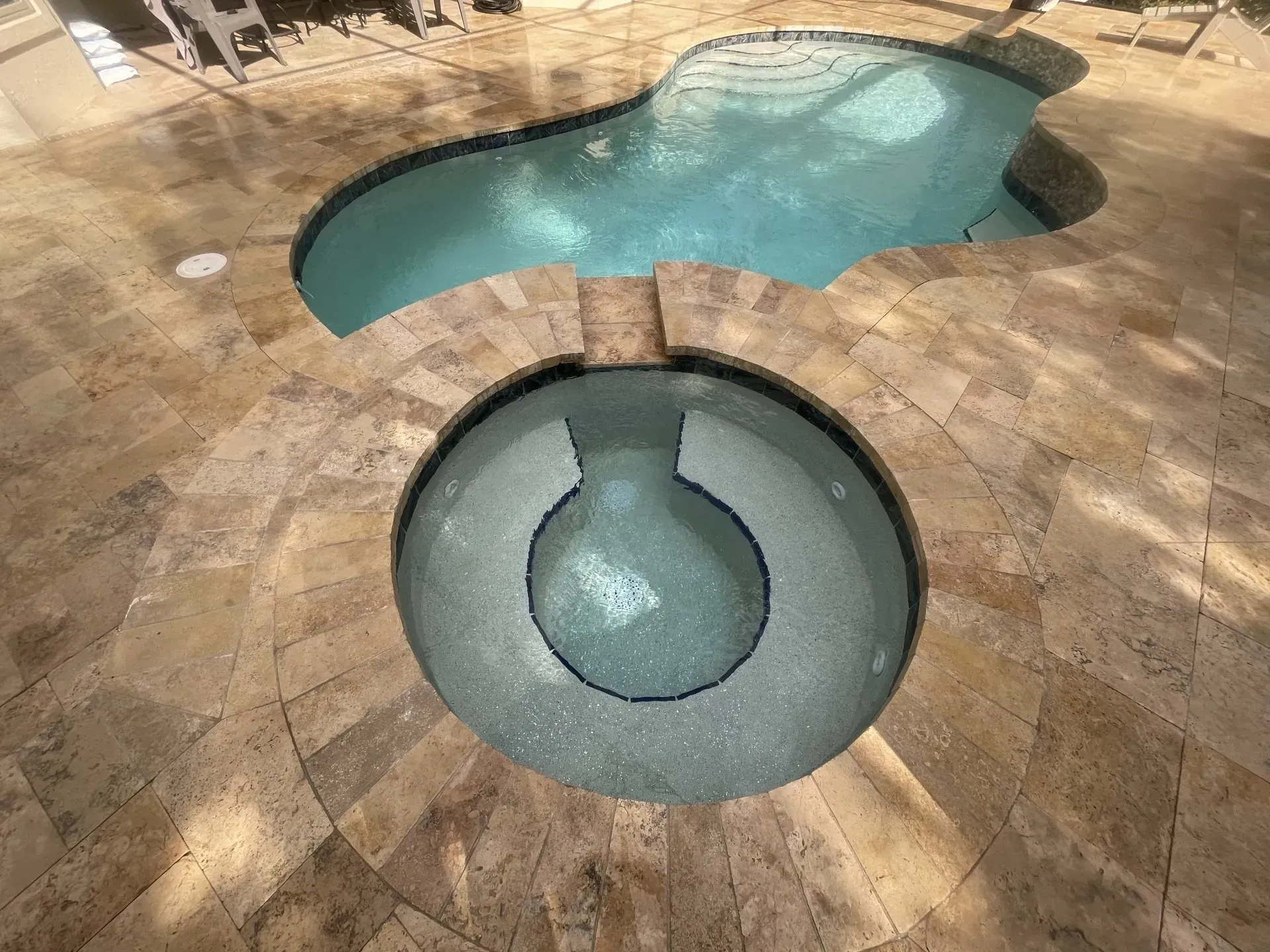 A pool and hot tub set into a stone patio. The pool is filled with clear water.