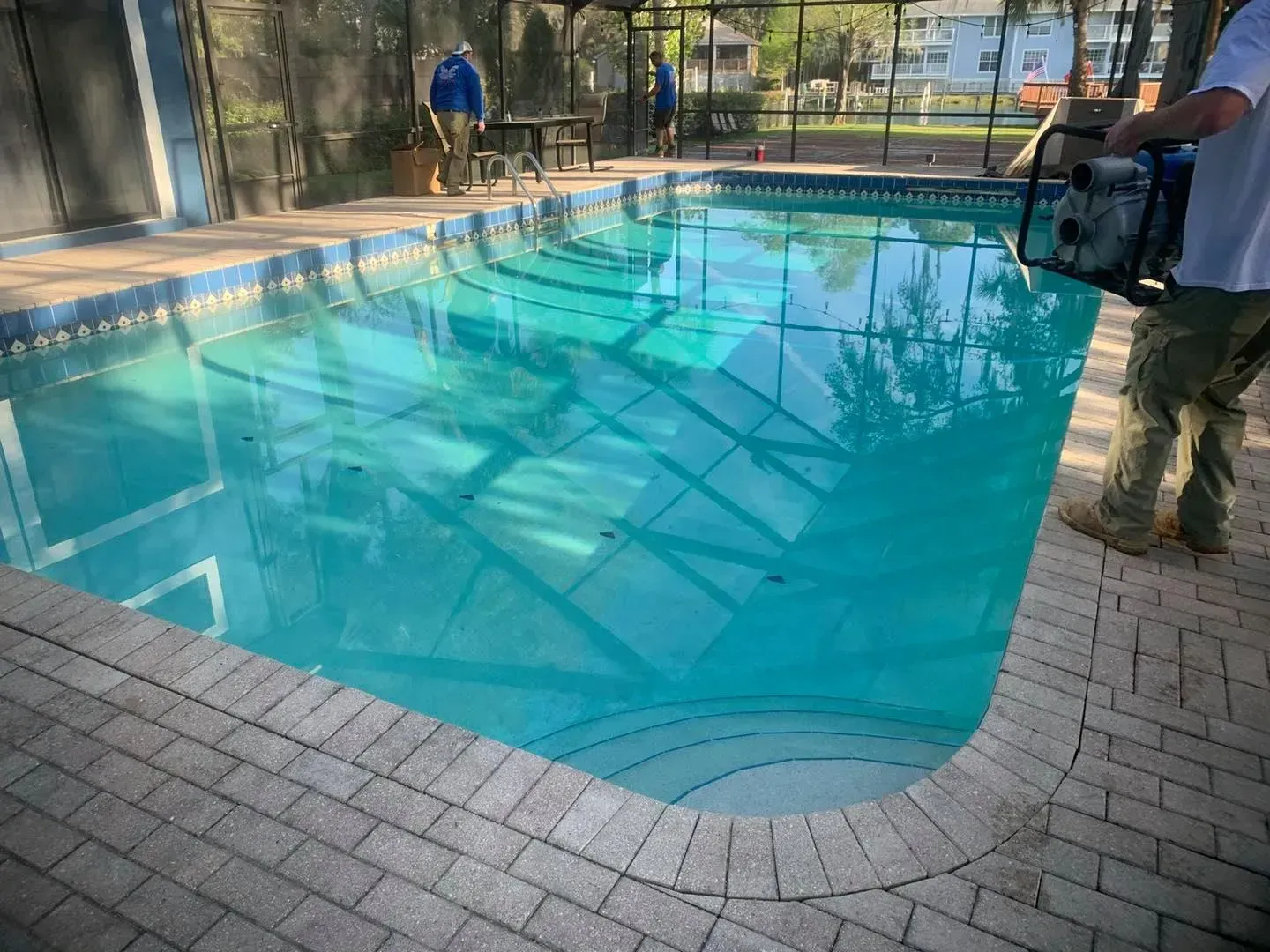 Pool being filled by a person with a pump. The pool has a brick border.