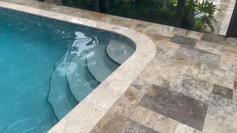 Pool with curved steps and stone coping, surrounded by stone patio.