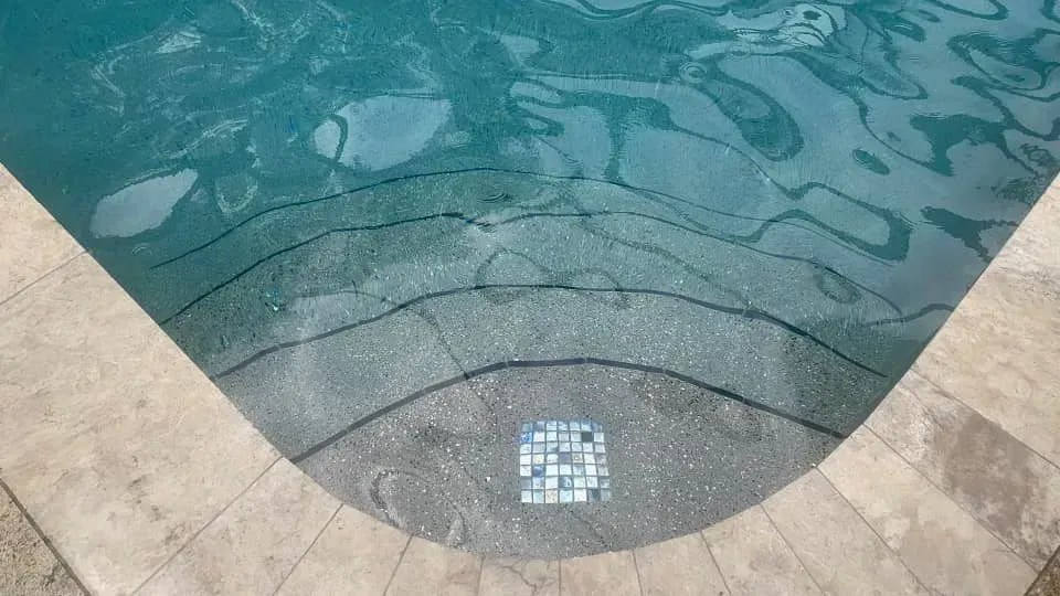 Pool steps submerged in clear blue water, with light tan stone edging.