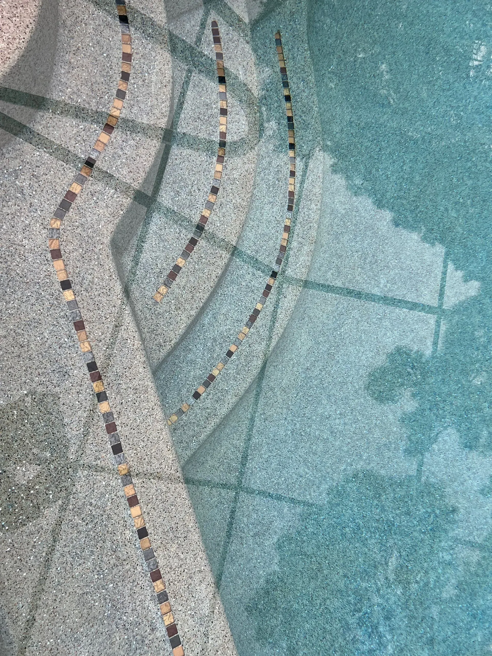 Pool steps with mosaic design, visible under the clear, blue water.