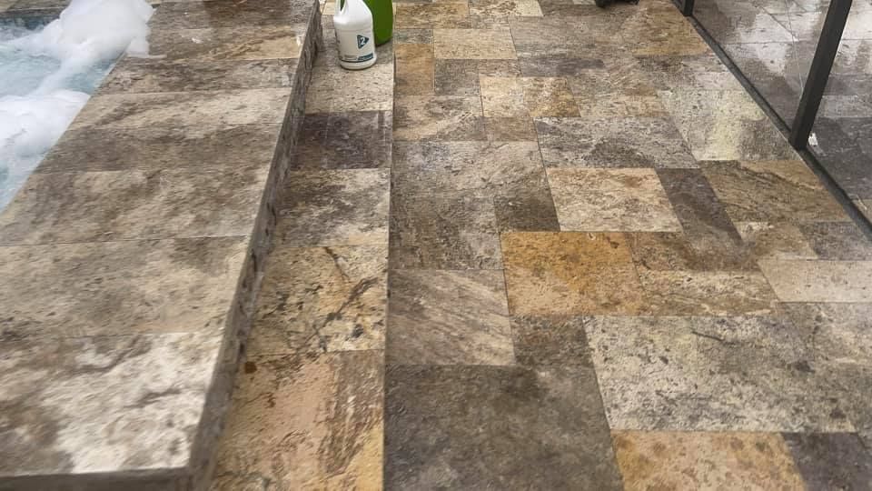 Stone tiled shower floor with steps, partially filled with bubbly water and a bottle.