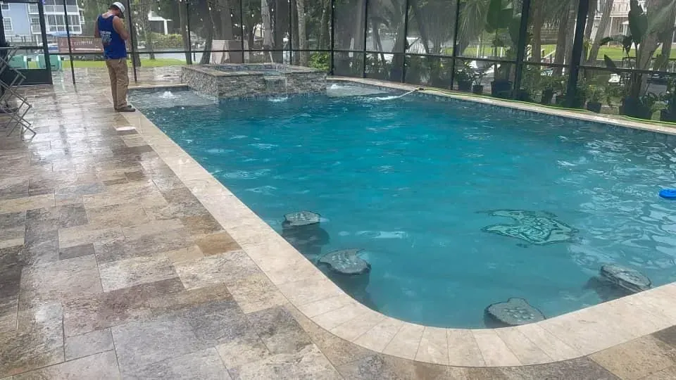 Outdoor pool with turquoise water, a hot tub, and stone coping; person standing near edge.