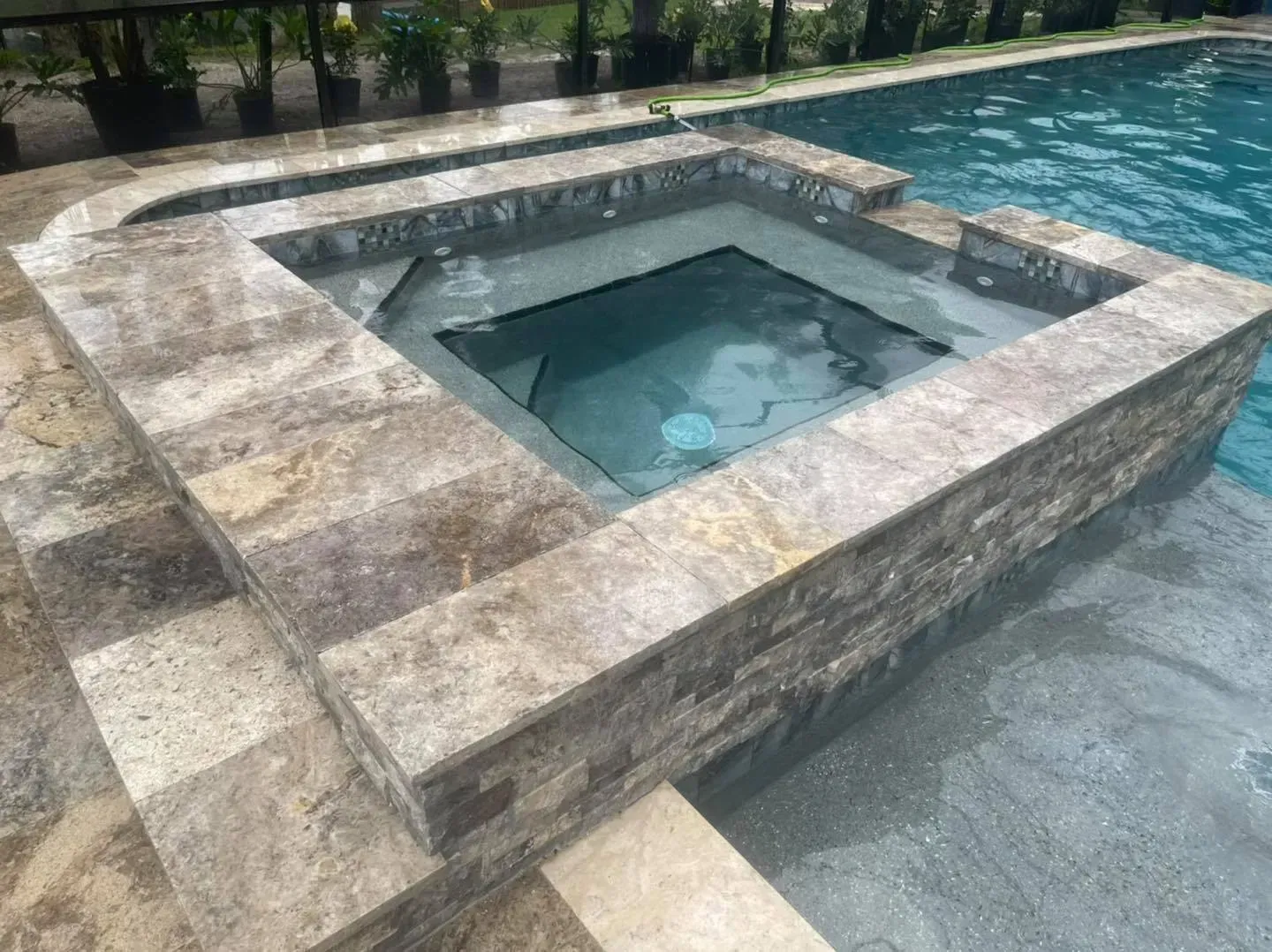 Pool and spa with tan stone border, blue water, and steps.