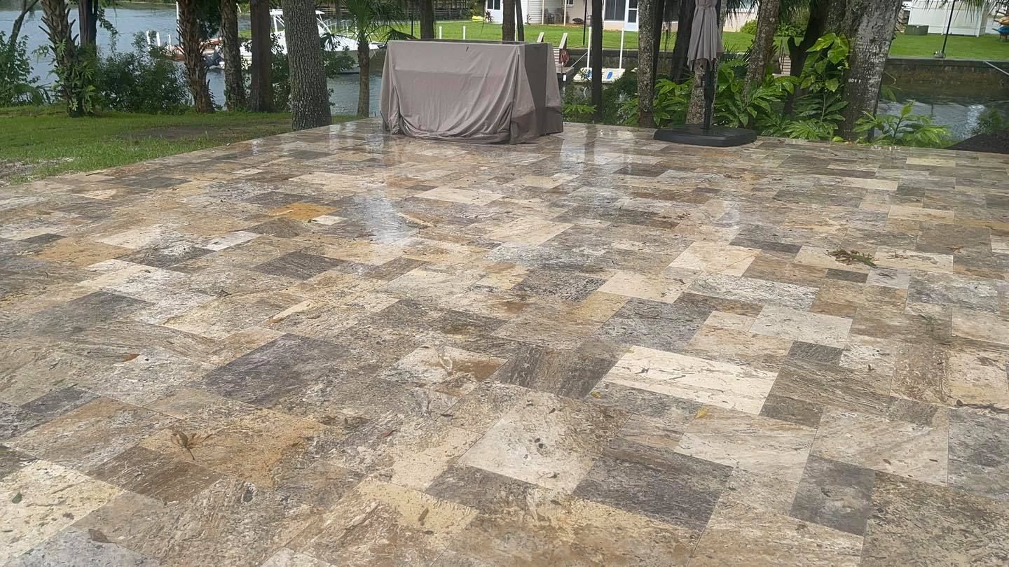 Patio with stone pavers wet after rain; trees and a lake in the background.