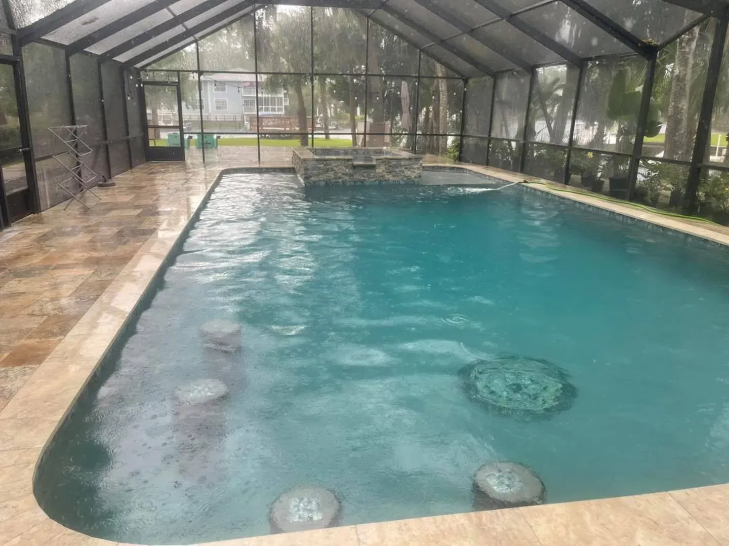Indoor swimming pool with turquoise water, screened enclosure, stone patio, and built-in bar stools.
