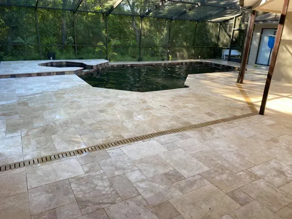 Stone patio with a dark-colored pool and hot tub, screened enclosure, and drain.