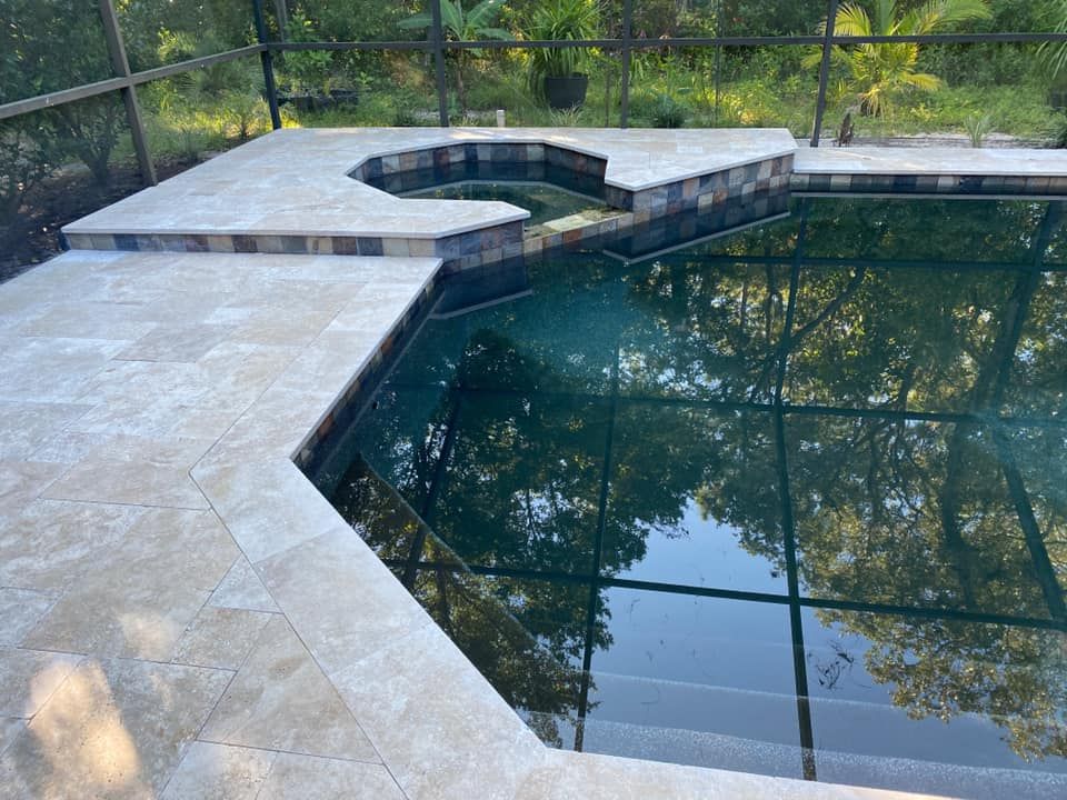Pool with stone coping and surrounding patio. Dark water reflects trees.