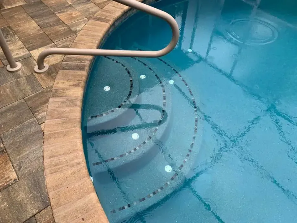 Pool steps with handrail, submerged lights. Steps have mosaic tile detailing, water is turquoise.