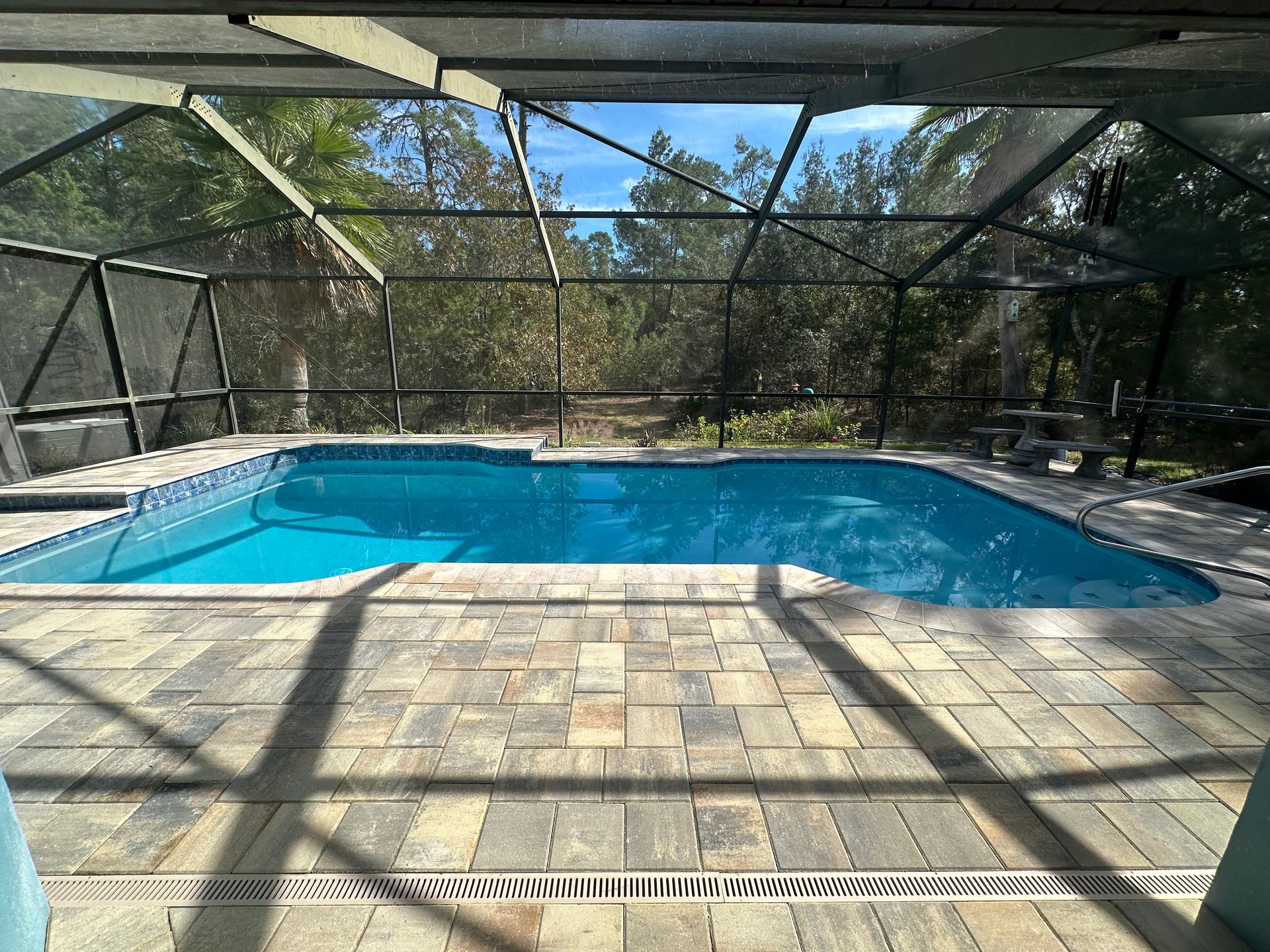 Screened patio with a blue swimming pool and gray paver deck beside a house