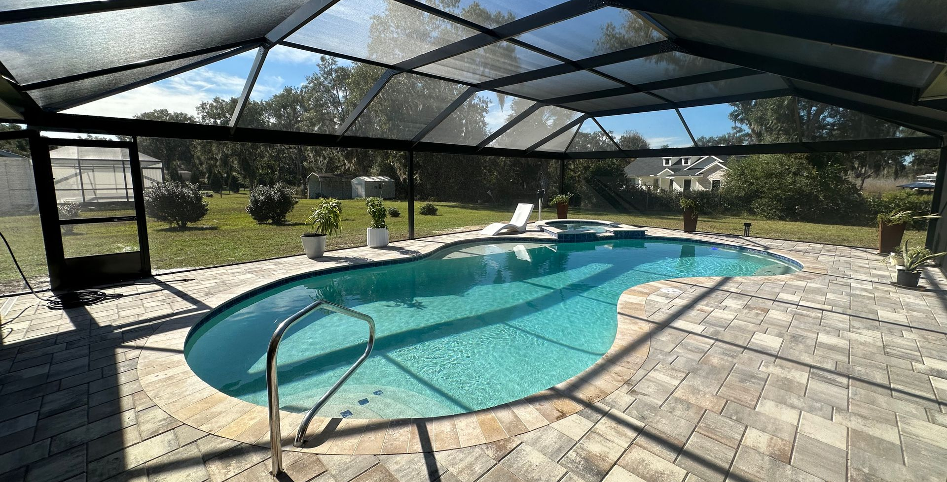 Screened-in backyard pool with turquoise water, stone deck, and lounge chairs under a patio enclosure