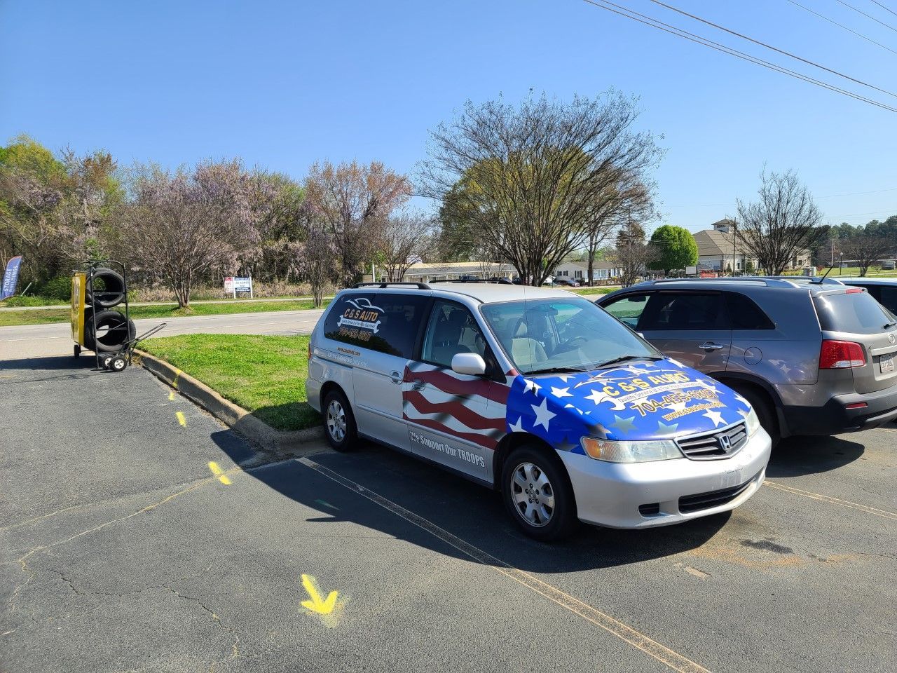 SUV wrapped in an American flag parked in a lot beside other cars and a grassy area