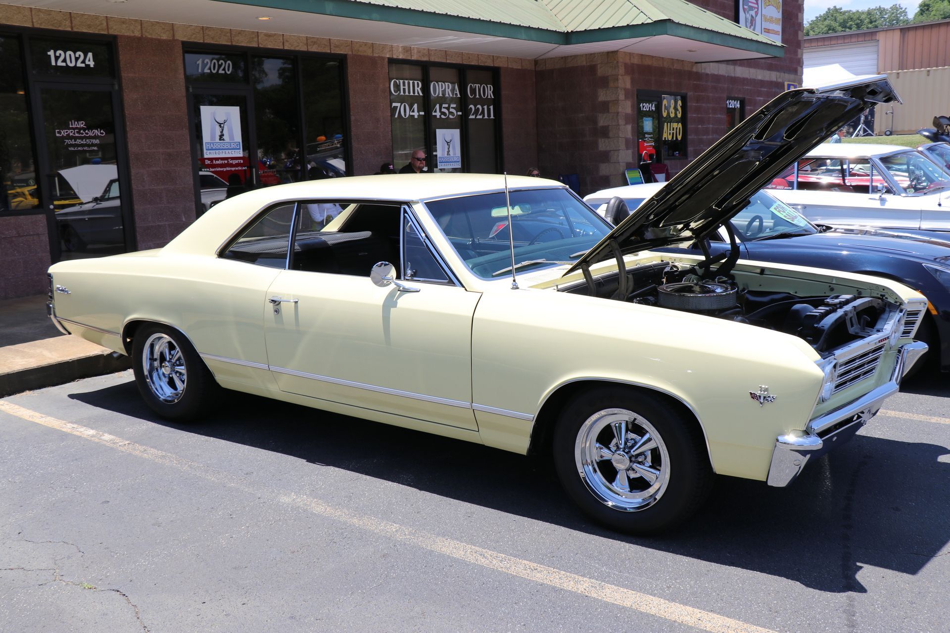 Classic cream-colored car with hood open, parked outside a storefront.
