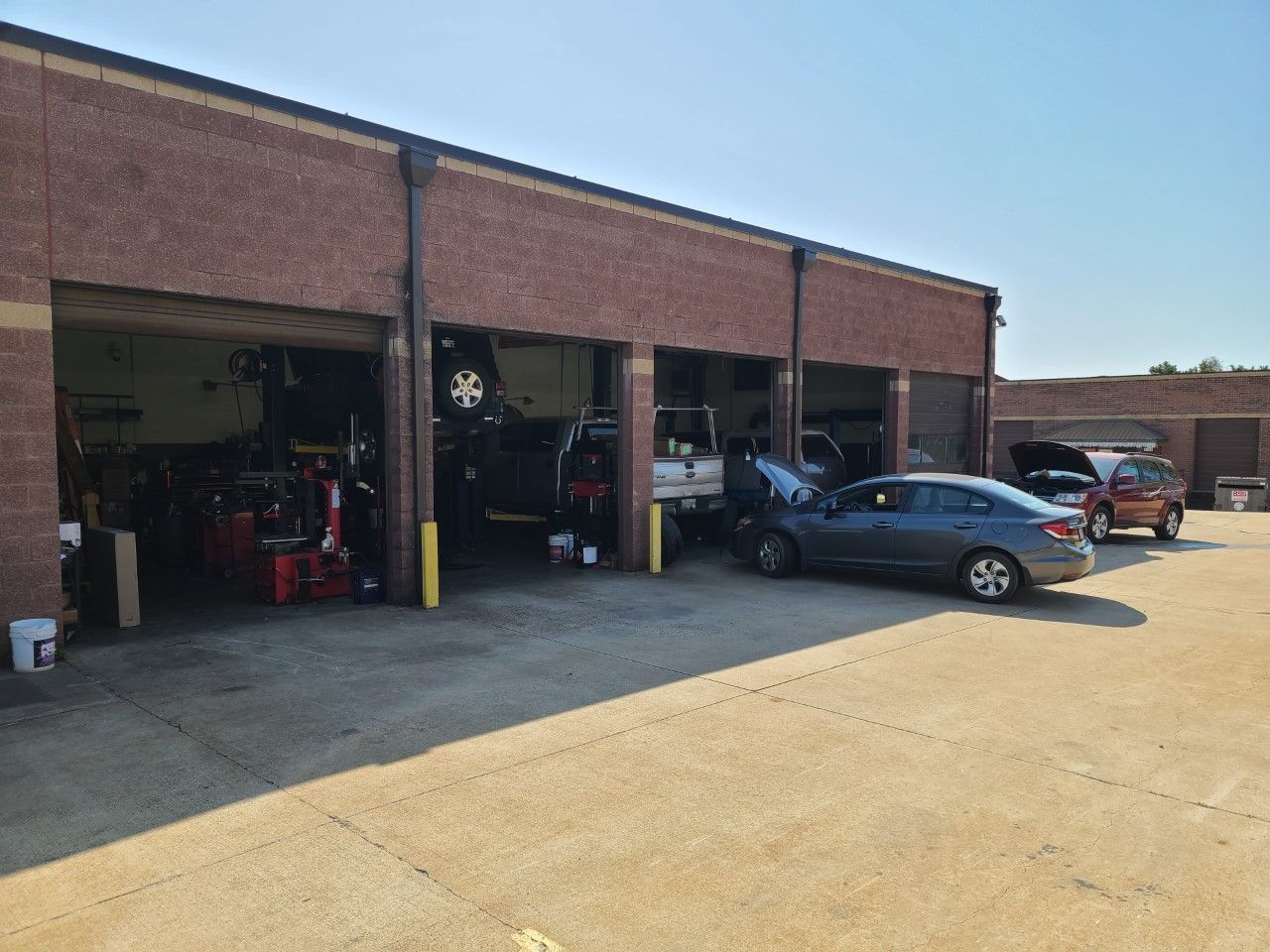 Auto repair shop with open garage bays and several cars parked outside on a sunny day