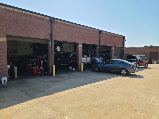 Auto repair shop with open garage bays and several cars parked outside on a sunny day