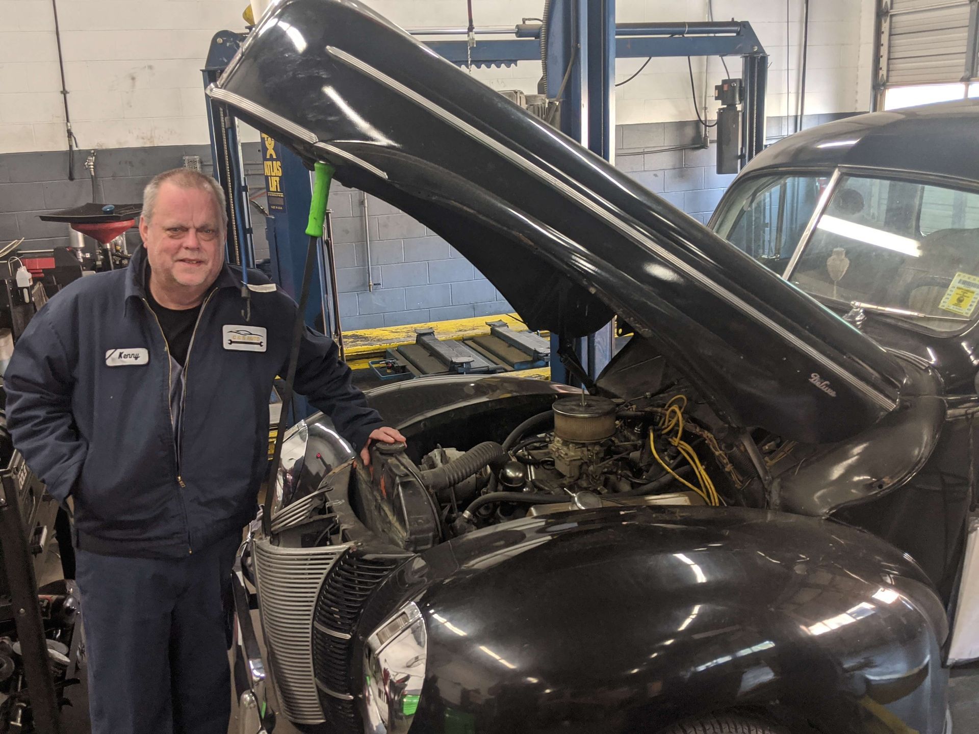 Mechanic beside a black car with hood open in an auto shop