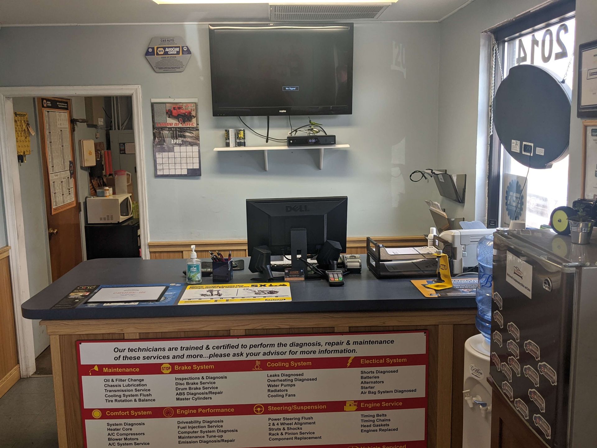 Front desk counter in a small office with a TV, computer monitor, and wall calendar behind it.