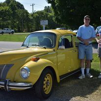 Yellow classic Volkswagen Beetle parked outdoors beside a person in shorts and a white shirt.