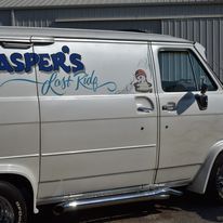 White van with “Jasper’s Lost Kids” logo and cartoon child on the side, parked by a building