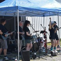 Band performing under a blue canopy tent on an outdoor stage