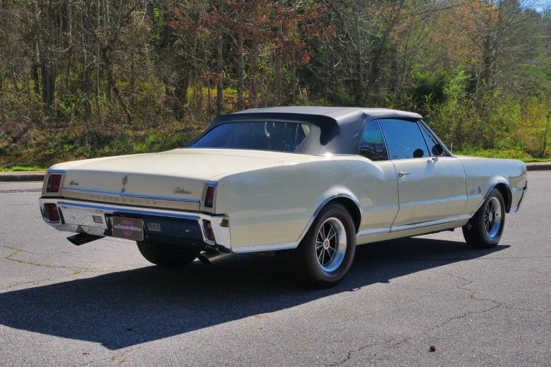 Classic cream-colored convertible car parked on a road with trees in the background