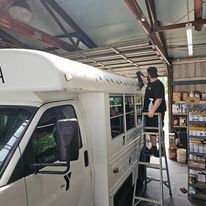 Person on a ladder installing lights on a white van inside a warehouse.