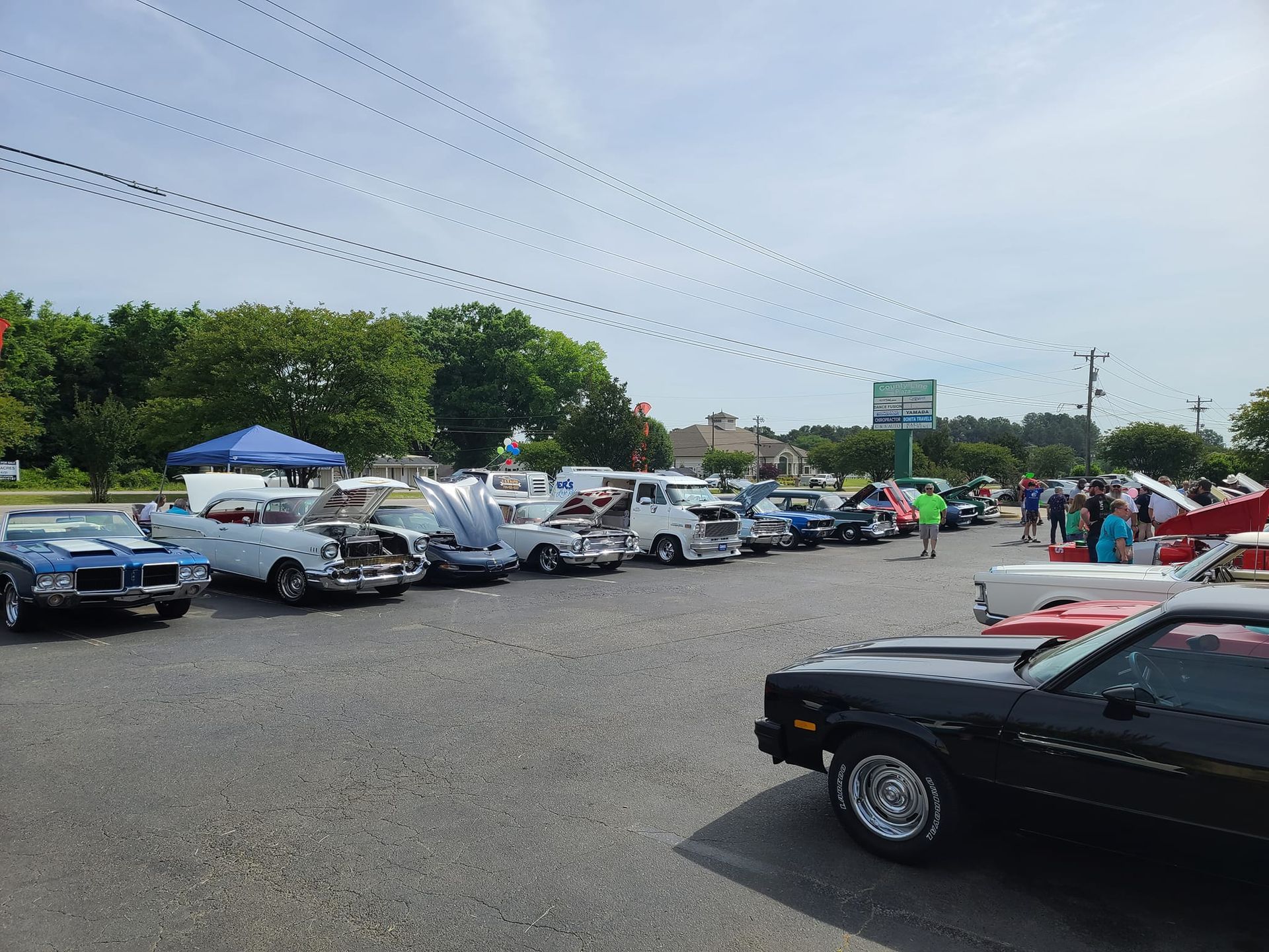 Outdoor car show with rows of classic cars parked on a gravel lot under a cloudy sky