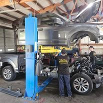 Mechanic working on a silver SUV on a lift inside an auto repair garage.