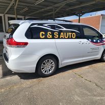 White minivan with “C&S AUTO” sign parked under a carport