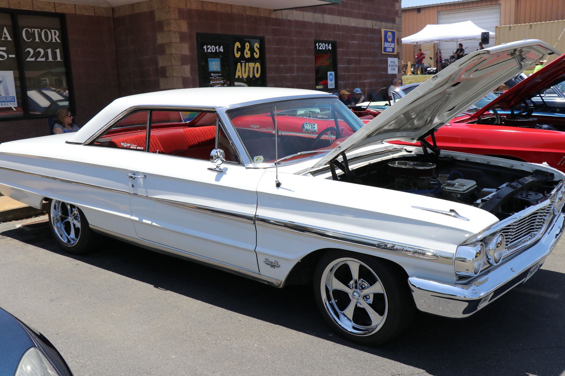 Classic white-and-red vintage car parked on street with hood open outside a brick building