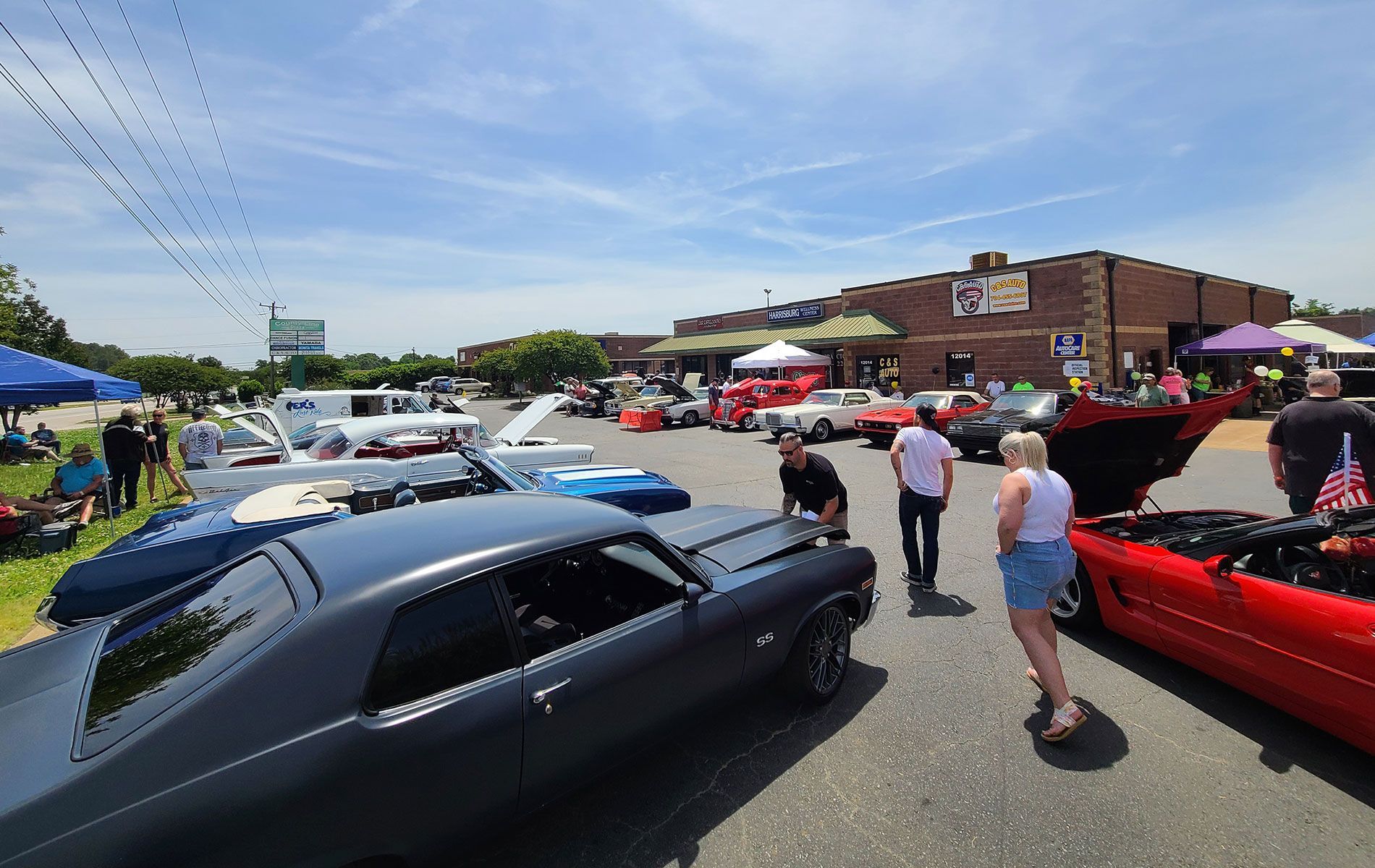Classic car show with black and red cars parked outside a brick building on a sunny day
