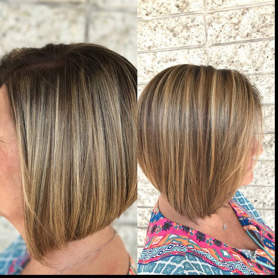 A woman with short hair is wearing a colorful shirt and standing in front of a brick wall.