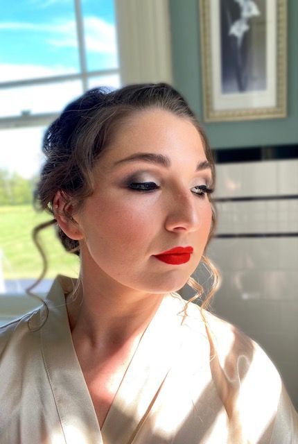 A woman wearing a white robe and red lipstick is sitting in front of a window.