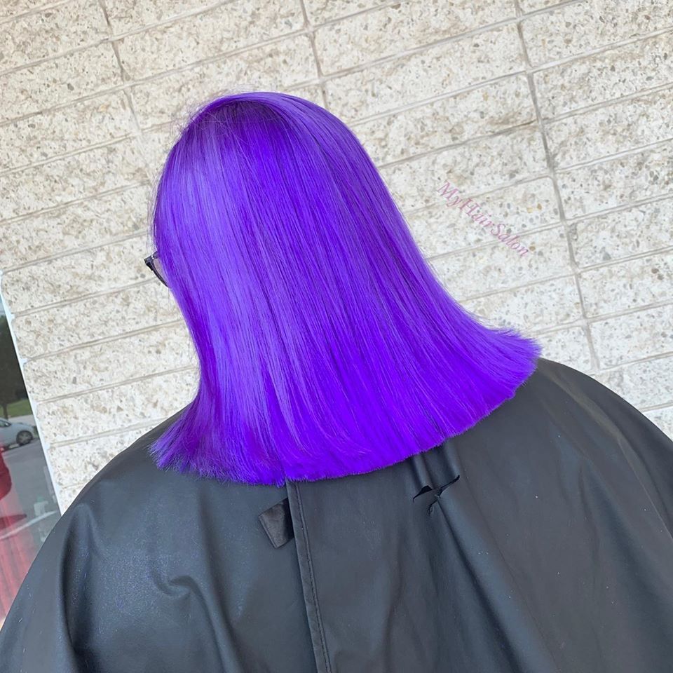 A woman with purple hair is wearing a black cape.