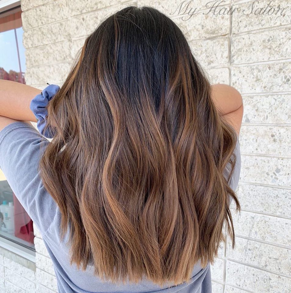 A woman with long brown hair is standing in front of a brick wall.