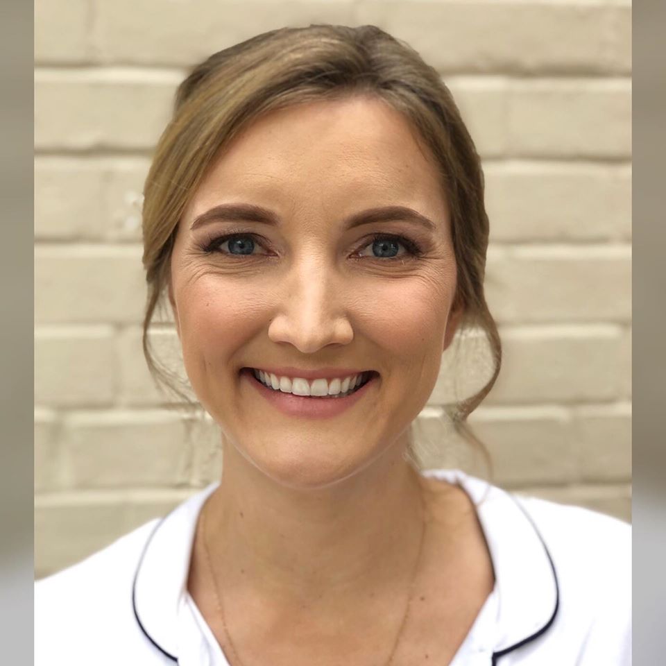 A woman is smiling in front of a white brick wall
