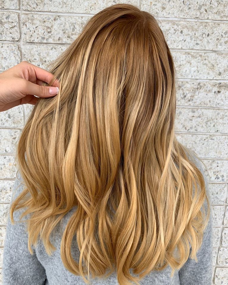 A woman with long blonde hair is standing in front of a brick wall.