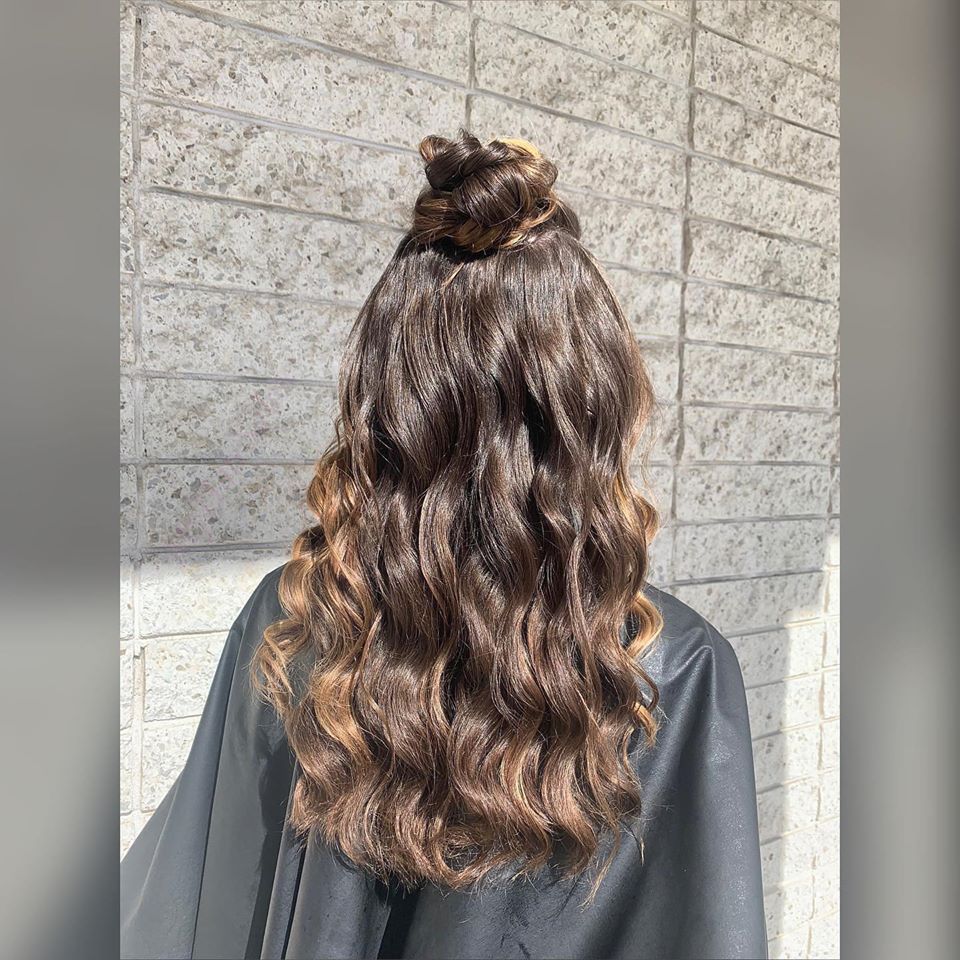 A woman with long brown hair is wearing a black cape and has her hair in a bun.